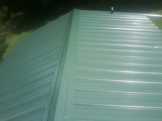 New green metal panels meeting at the ridge of a roof — Flat Roof Repair work by our crew in Lowell